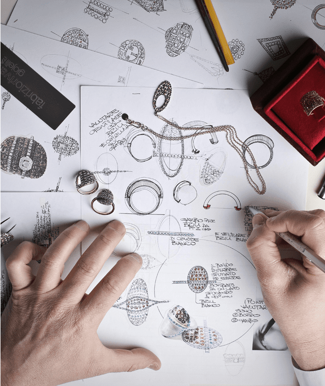 A person drawing on paper with some jewelry.